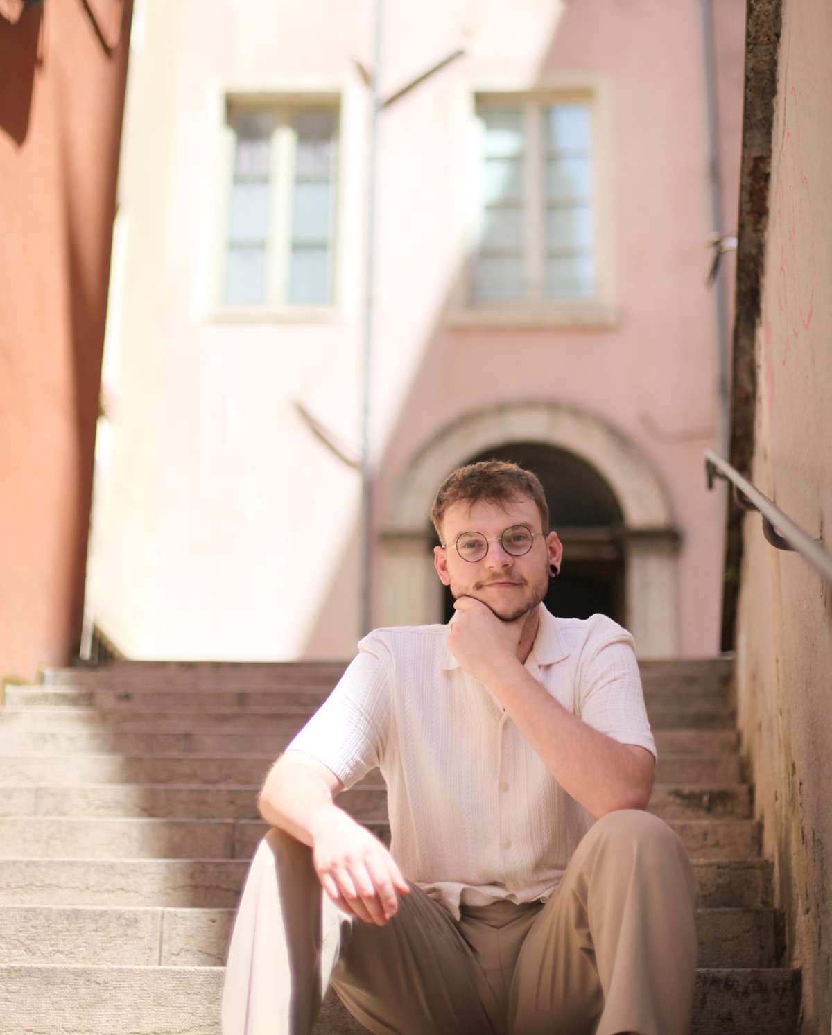 Antoine assis sur des marches devant une façade rose